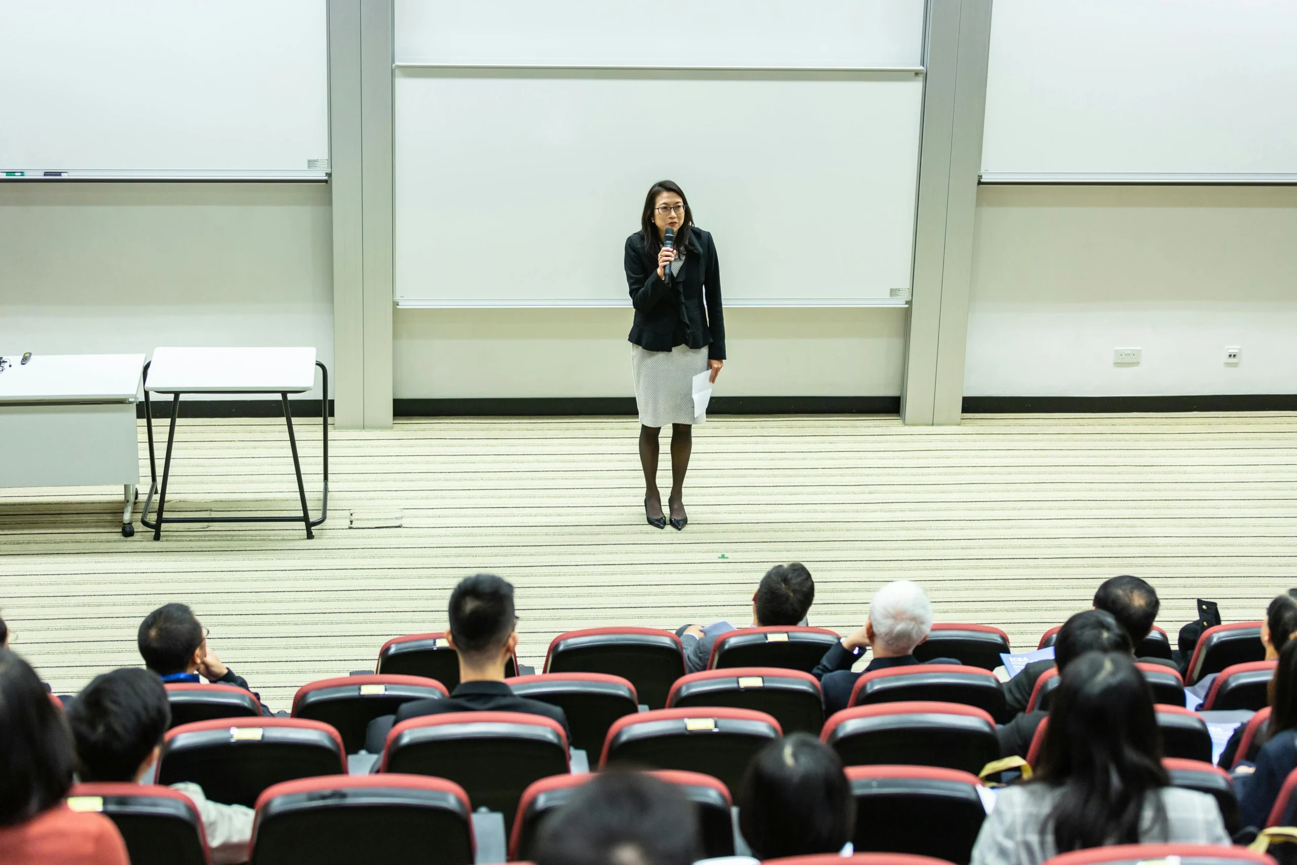 Woman speaking confidently to an audience in a lecture hall showing how to be confident in public speaking.