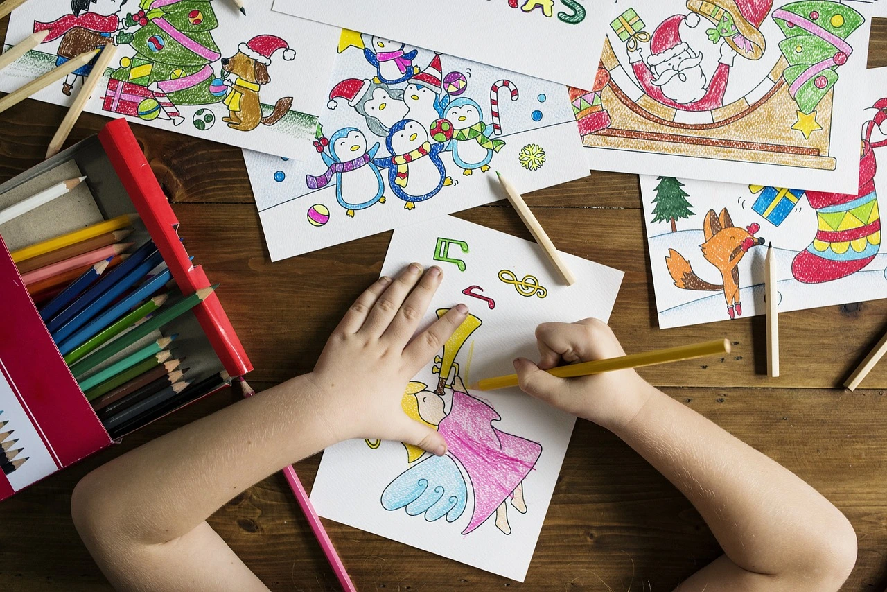 Child coloring festive drawings with colored pencils on a wooden table during a drawing activity.