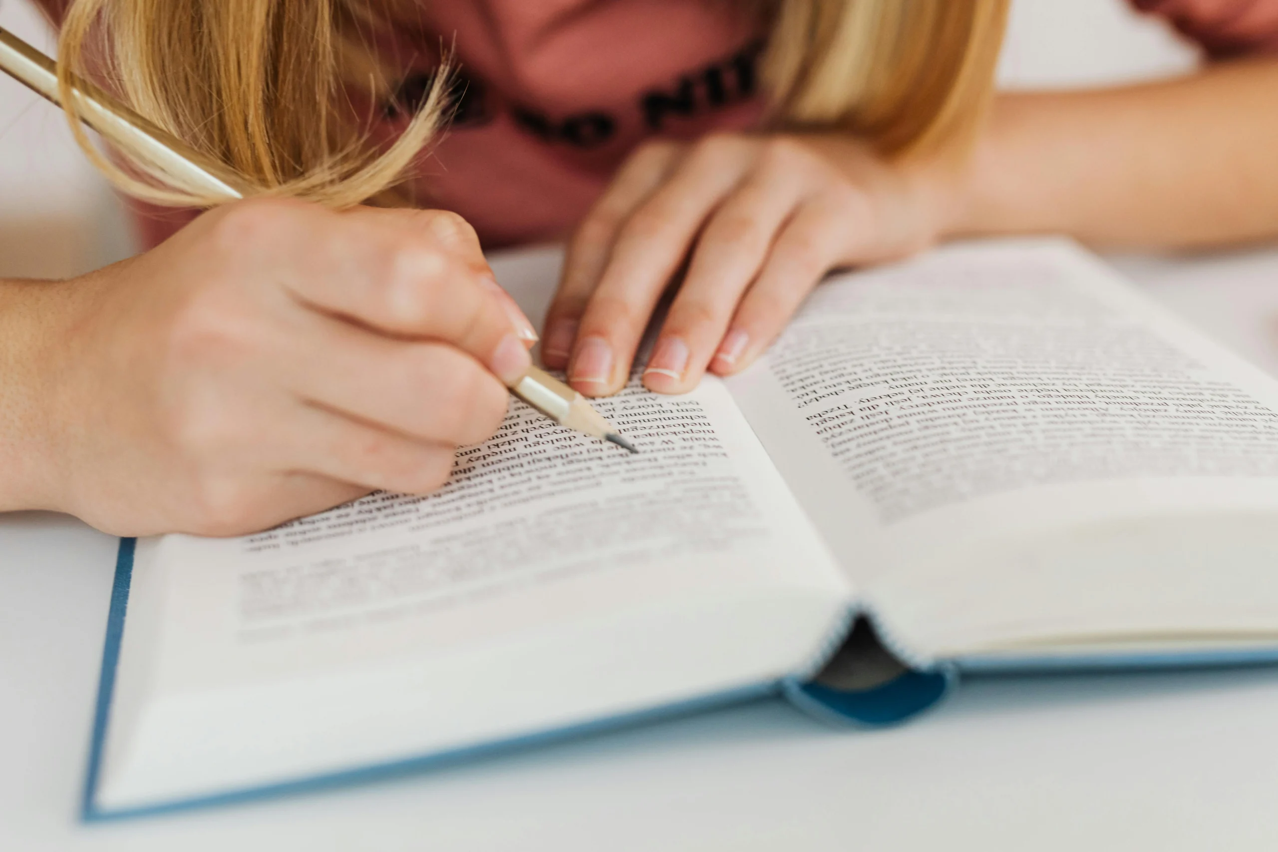 Person taking notes in an open book, representing study and research for essay writing topics